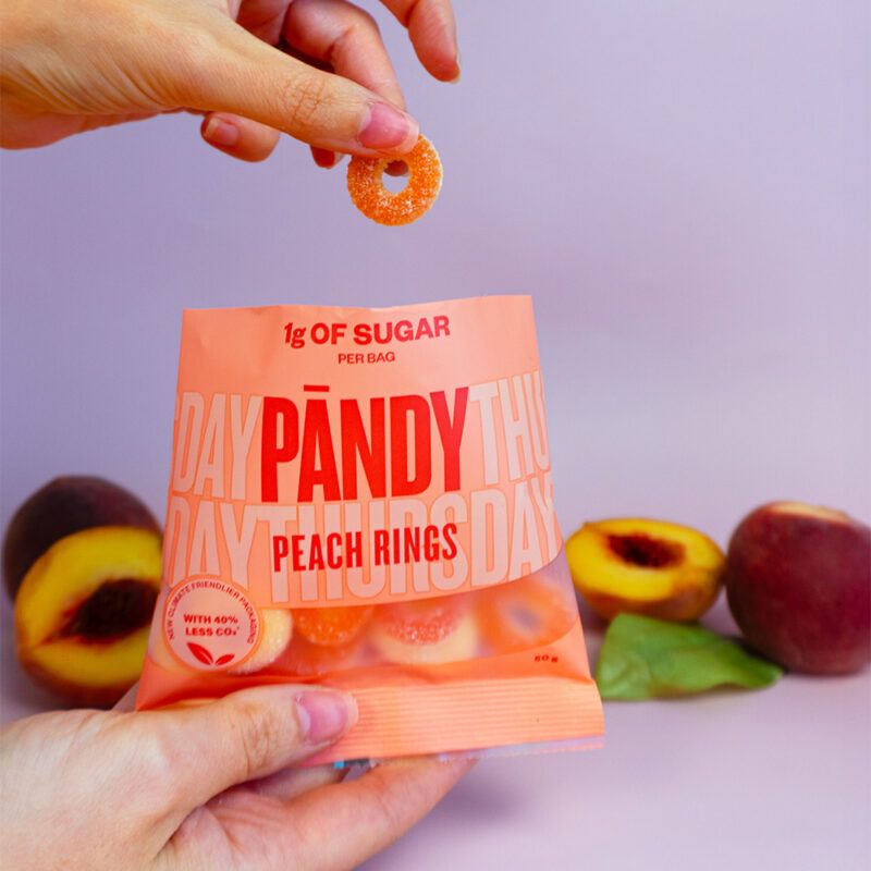 En hånd tager en Pandy Candy Peach Ring vingummi op af en pose.