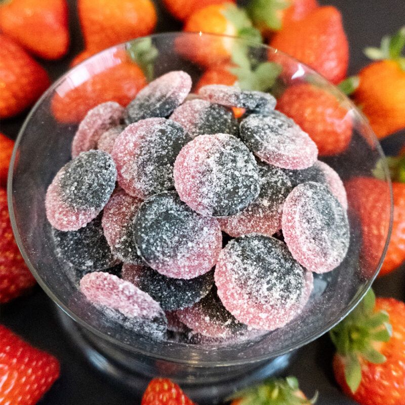Skål med Pandy Candy Strawberry Liquorice med en baggrund af jordbær.